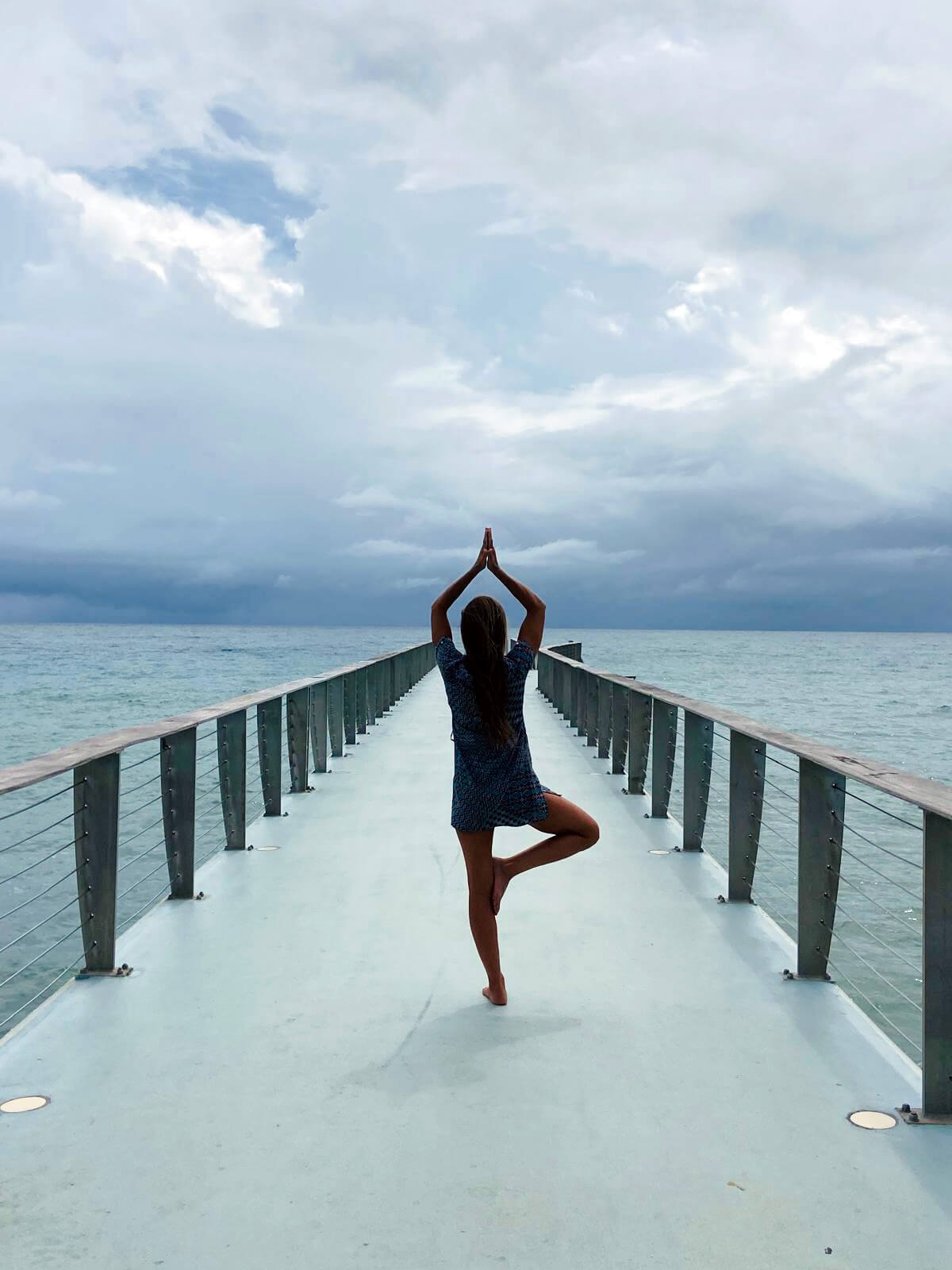 Isa fait la posture de l'arbre sur un ponton, entourée par l'eau