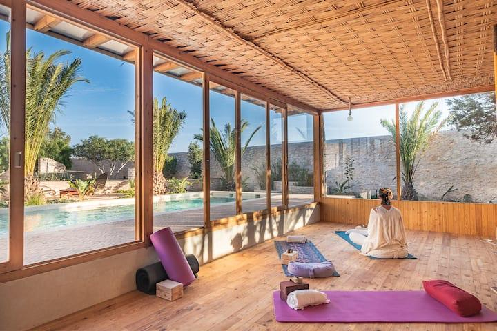 Femme médite dans une salle de yoga face à la piscine de l'ecolodge d'Essaouira