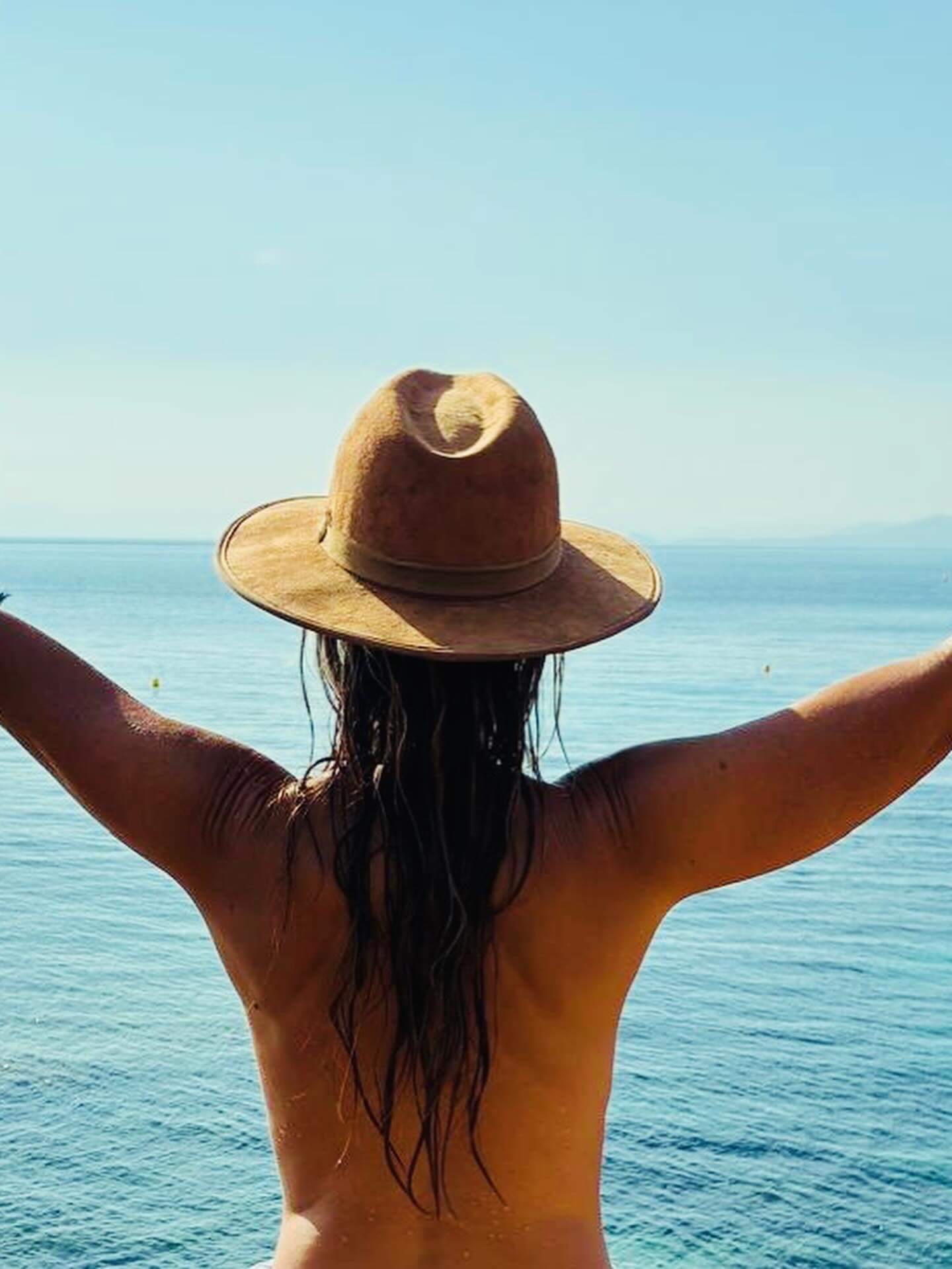 Isa nue de dos avec chapeau, face océan